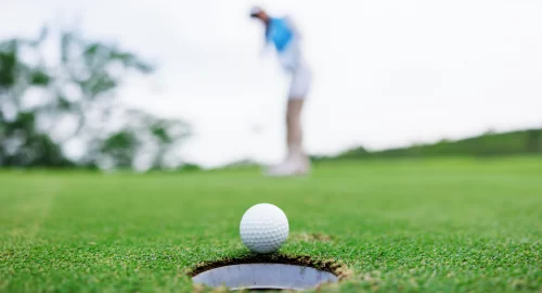 Golf ball at the edge of the hole on the greens with a blurred background of golfer in the back