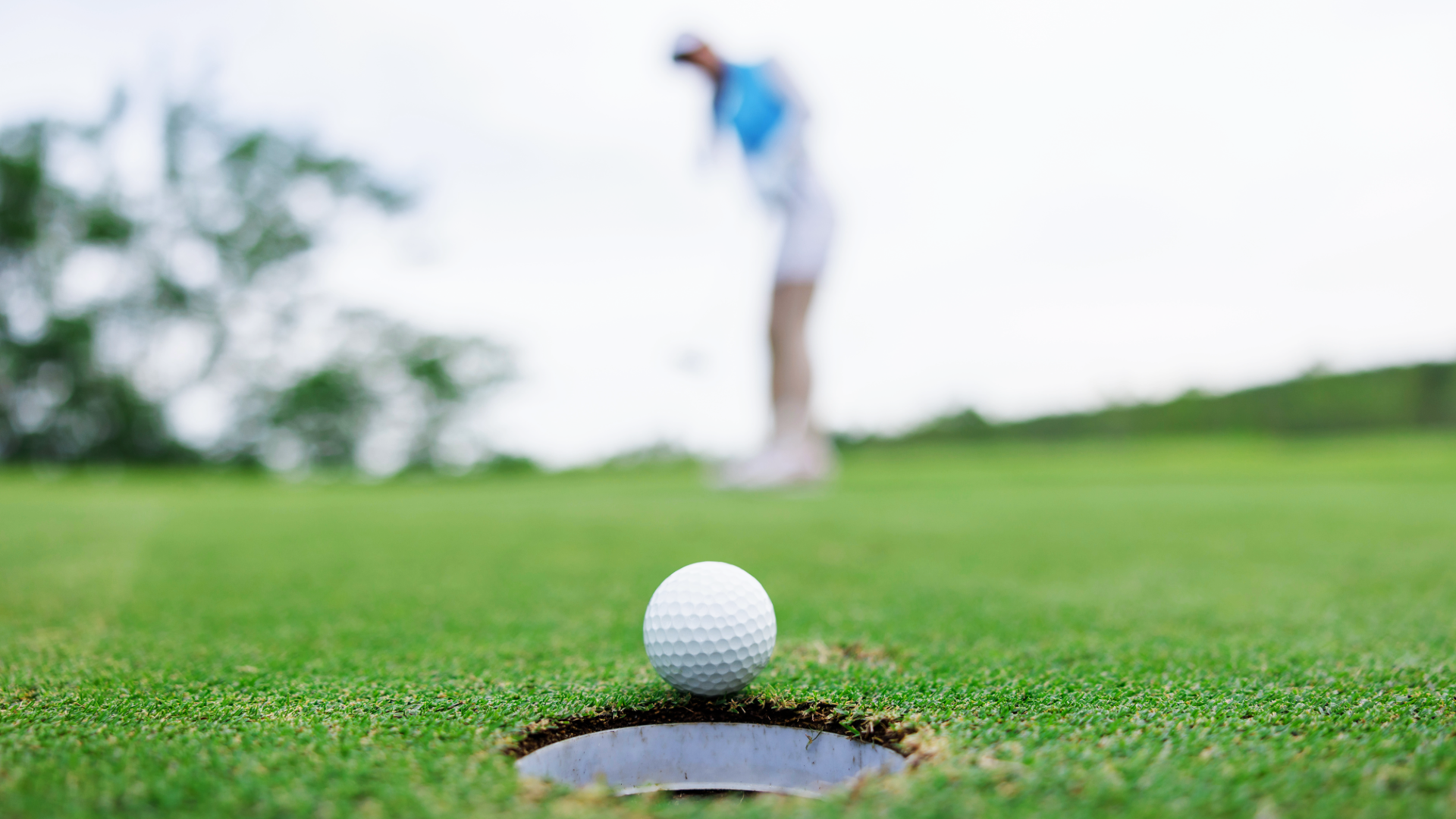 Golf ball at the edge of the hole on the greens with a blurred background of golfer in the back