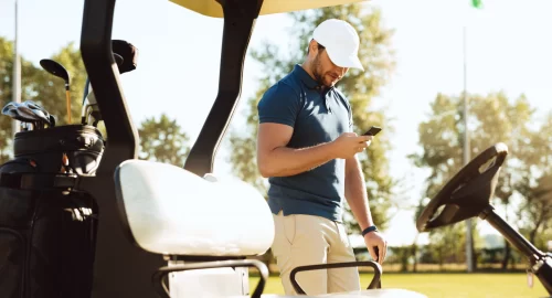 Golfer looking at phone next to golf cart
