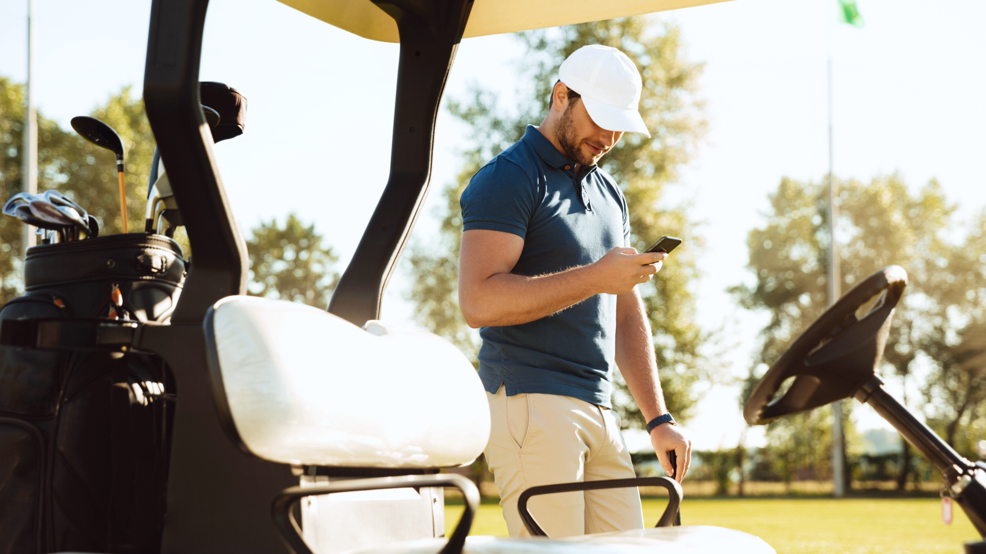 Golfer looking at phone next to golf cart