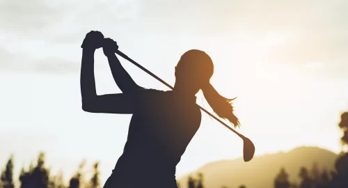 Silhouette of a woman on the golf course, mid golf swing.