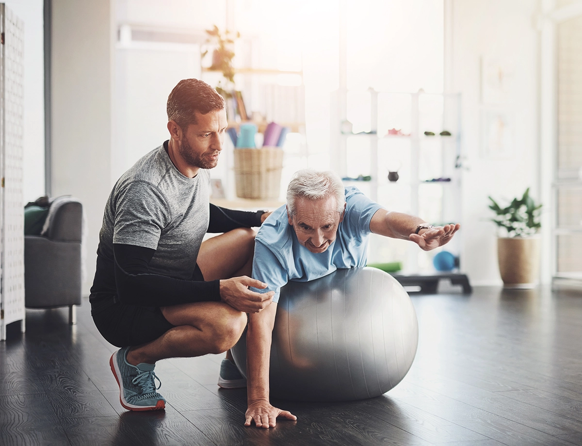 Image of a senior on a balance ball struggling with a trainer