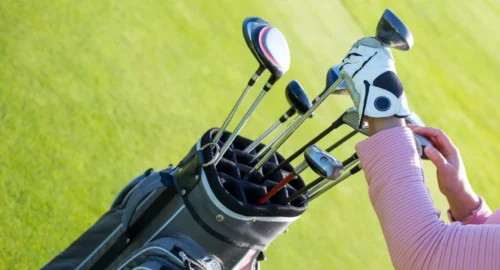 Close up shot with a person with golf gloves on pulling clubs out of a golf clubs bag on the golf course.
