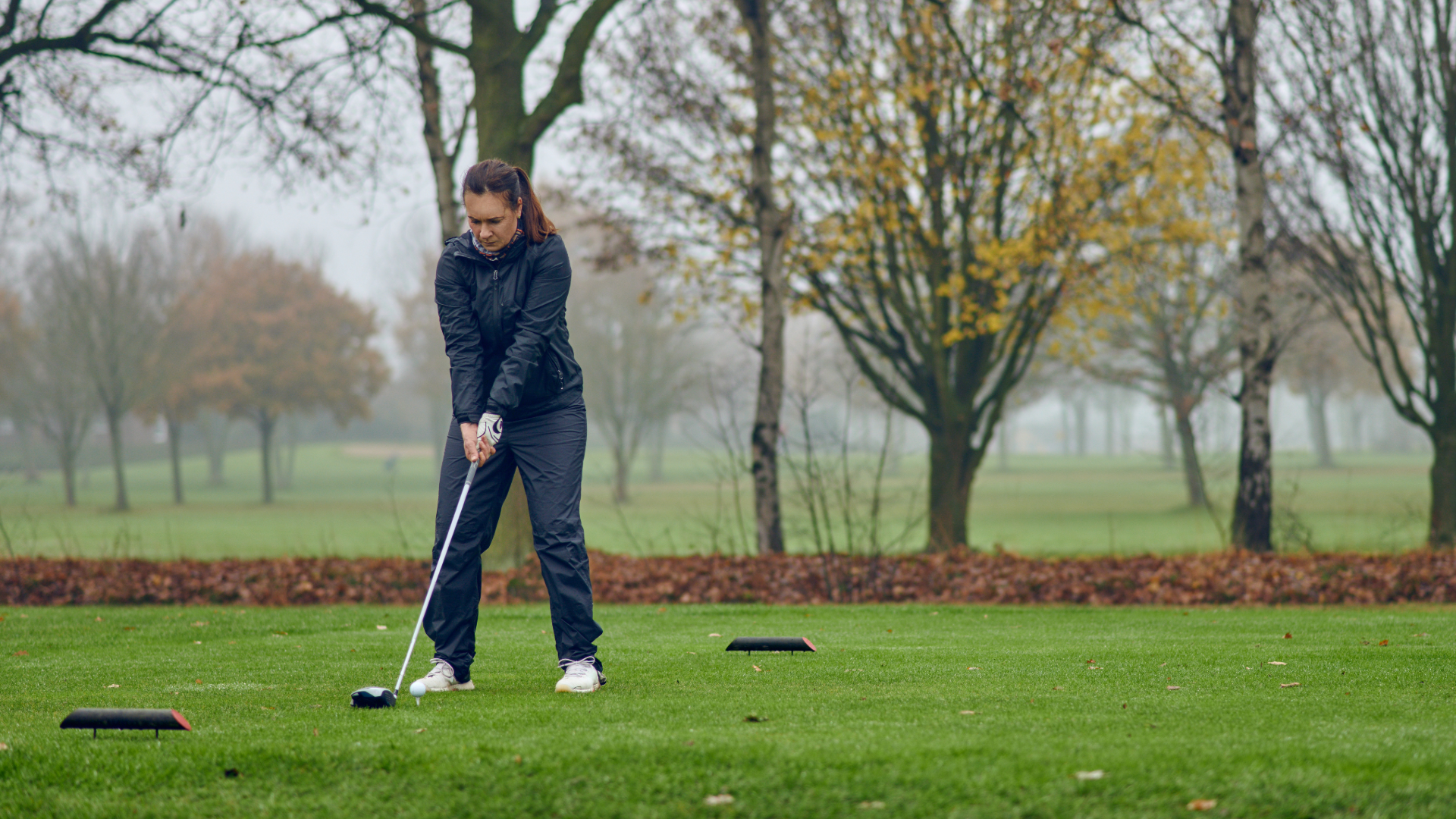 A woman on the golf course, practicing in misty, cold weather with the appropriate rain gear.
