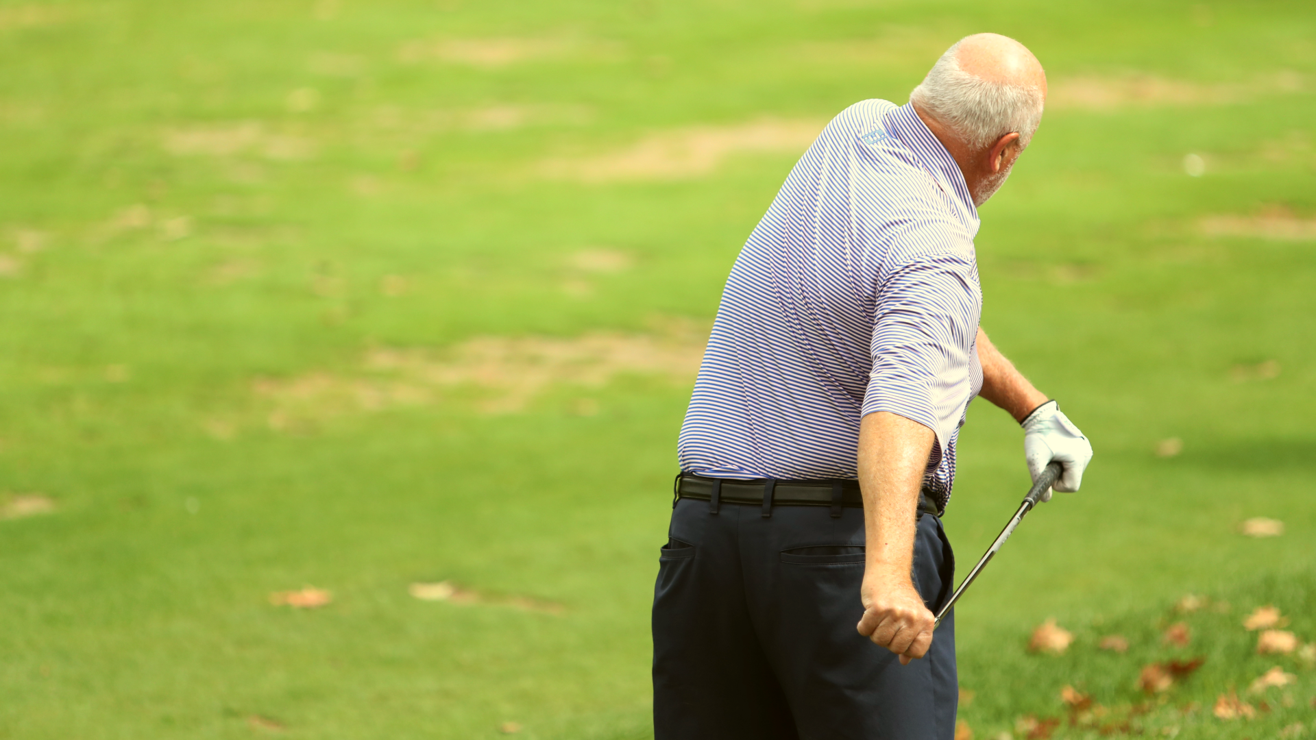 A golfer on the course, holding a golf club in both hands and twisting in a stretching exercise.