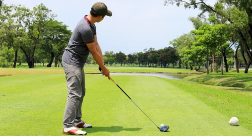A Golfer on a course looking toward a water obstacle, setting up their golf swing.