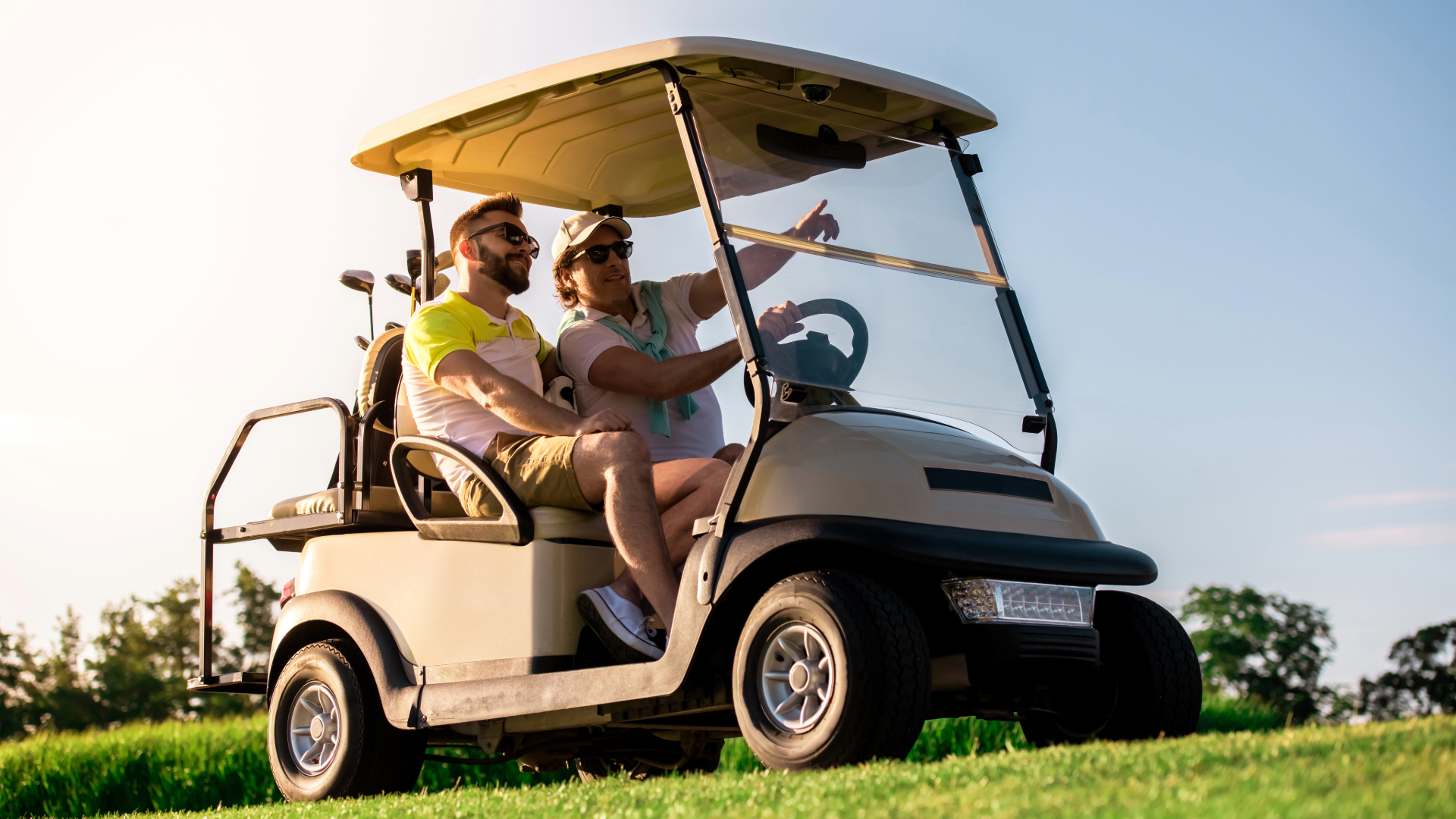 Two men in a golf cart, pointing to something on the golf course.