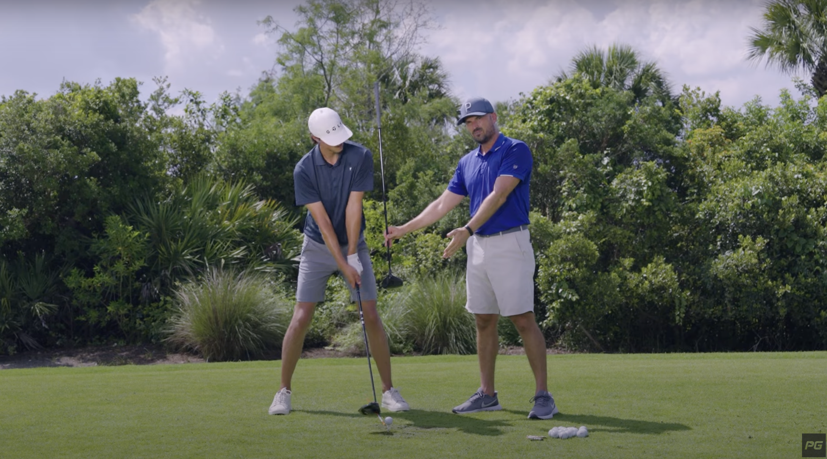 Grant Horvat setting up for the driver swing, with Eric Cogorno holding up his club to emphasize his shoulder lean and the proper ball position and setup.