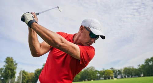 Close up of a man on the golf course mid-golf swing.