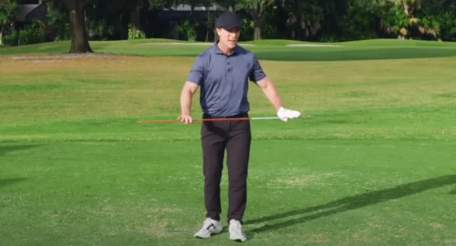 Performance Golf coach holding an alignment stick perpendicular to his torso to show how you can use this training aid to keep a narrow stance and rotate your torso from left to right.
