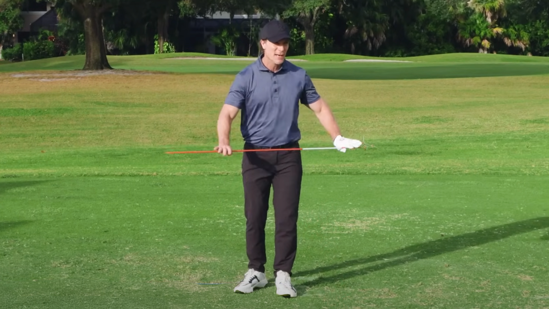 Performance Golf coach holding an alignment stick perpendicular to his torso to show how you can use this training aid to keep a narrow stance and rotate your torso from left to right.