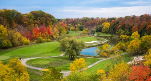 A golf course during the fall with orange and yellow foliage, a pond and a bunker.
