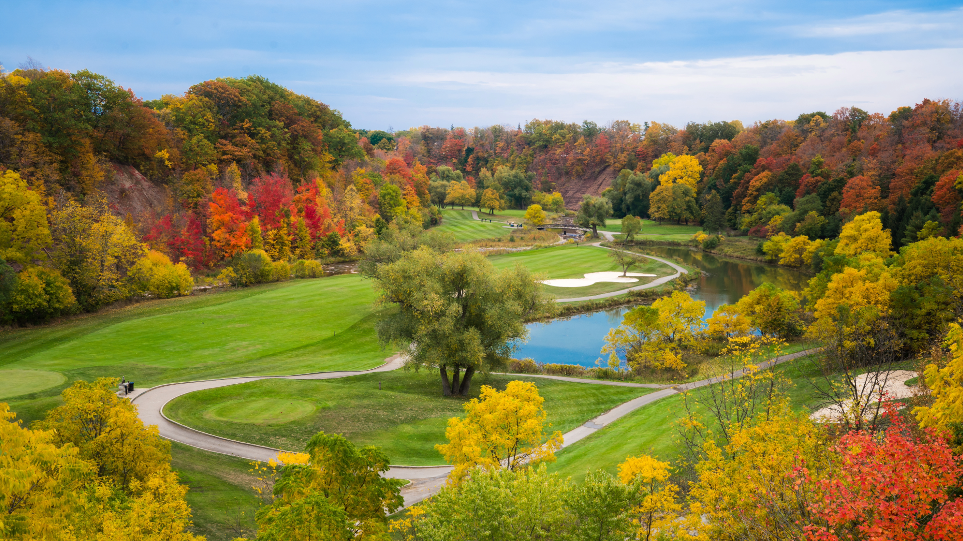 A golf course during the fall with orange and yellow foliage, a pond and a bunker.