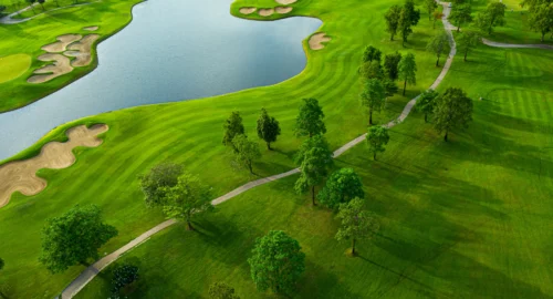 An aerial view of a golf course, with a winding path, trees, bunkers and water features.